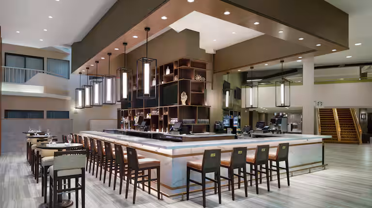 Bar contemporain du DoubleTree by Hilton Newark Penn Station, avec un long comptoir élégant, des tabourets modernes, un éclairage suspendu design et une ambiance chic et conviviale au cœur de l’hôtel.