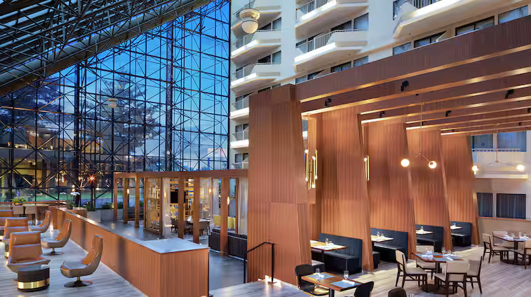 Lobby moderne et lumineux du DoubleTree by Hilton Newark Penn Station, avec de hauts plafonds vitrés, des structures en bois au design contemporain, des espaces lounge élégants et un coin bar-restaurant à l’ambiance chaleureuse.